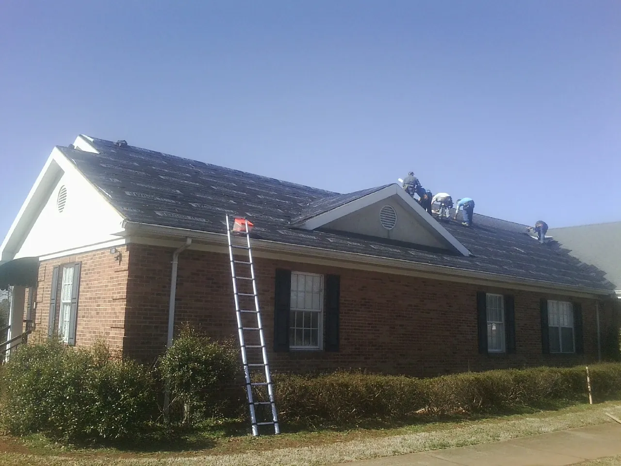Crew tearing shingles off a brick ranch roof with a ladder set — Metal Roof Repair work by our crew in Pleasant Ridge