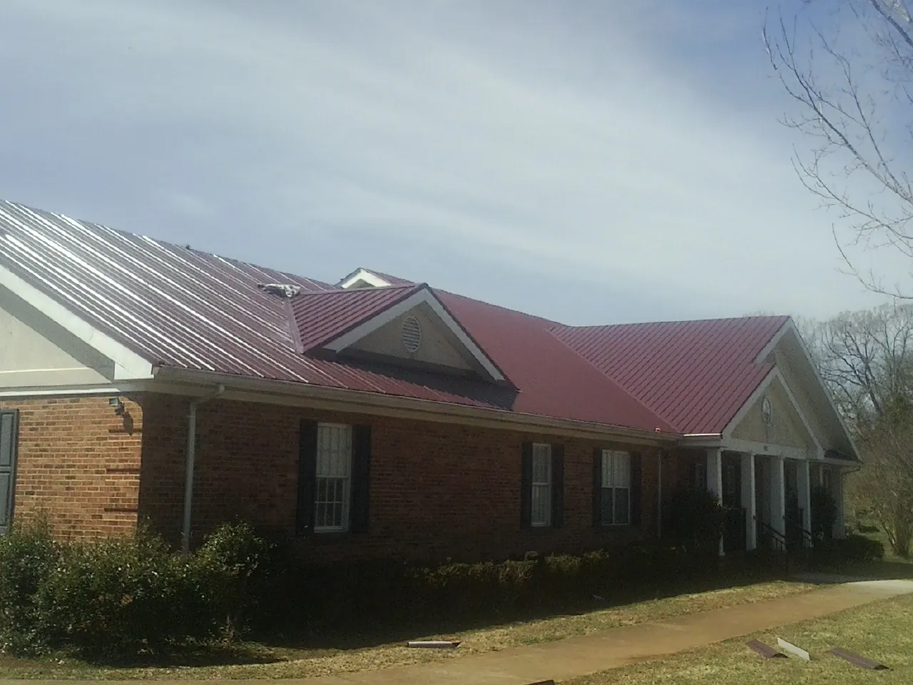 Red metal roof with gabled entries on a long brick building, from a Hail Damage Roof Repair job in Pleasant Ridge