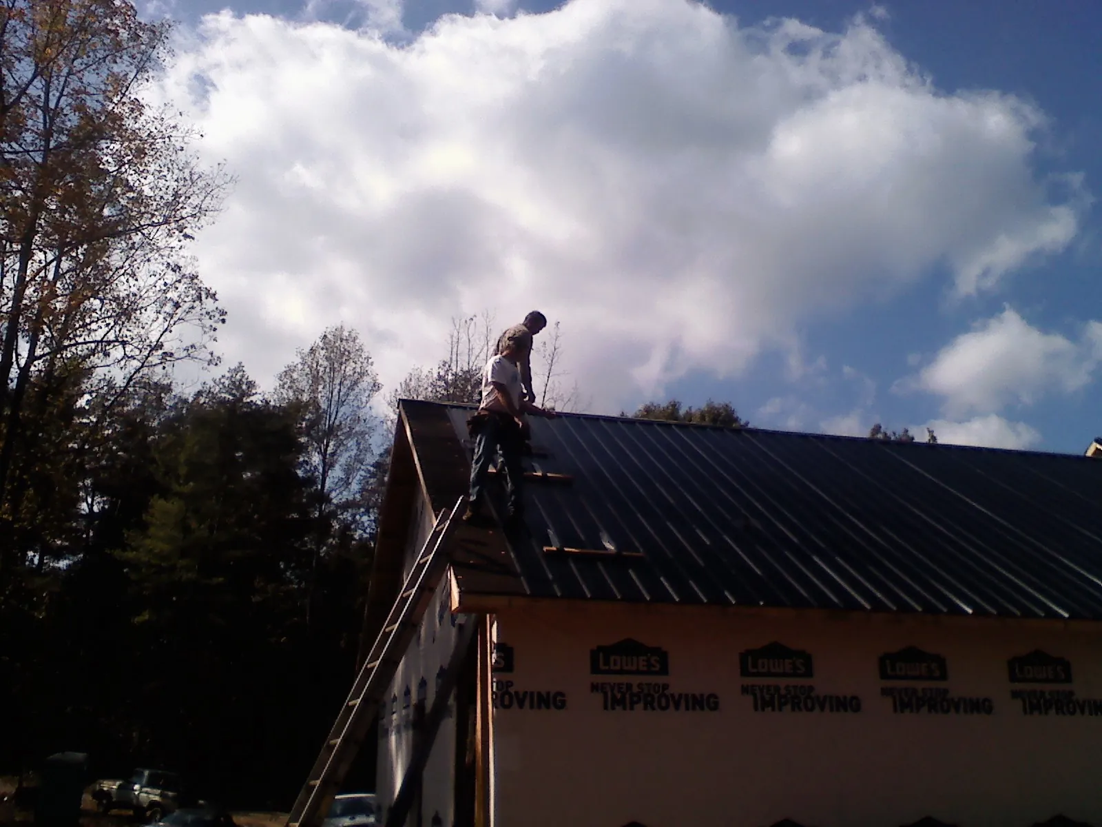 Roofer fastening dark metal panels high against a cloudy sky, from a Roof Inspection job in Pleasant Ridge