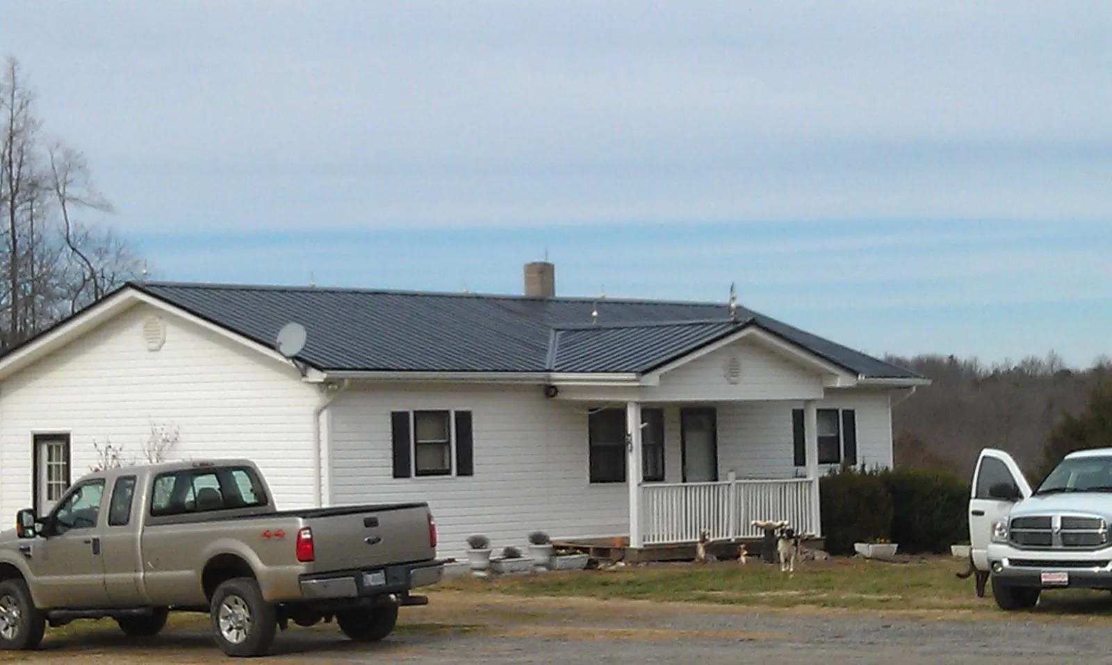 Finished dark metal roof on a white ranch home with work trucks parked in Pleasant Ridge