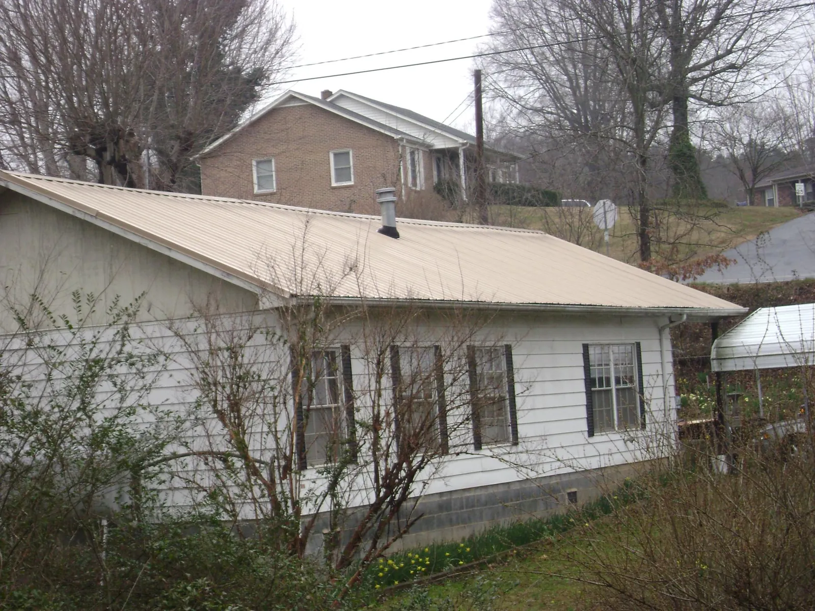 Tan metal roof on a white sided house set into a hillside — Commercial Roofing by Roofing Brothers in Pleasant Ridge